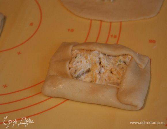 Смазываем края булочек желтком, взбитым с водой и сворачиваем во внутрь так, чтобы начинка осталась открытой.