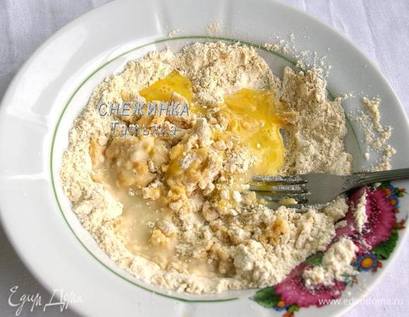 Затем в эту муку добавьте 2 ч. л. сливочного масла, половину яйца и воду. Для тех, кто не знает, как отмерить половину яйца: яйцо разбейте в чашку, слегка взбейте и используйте необходимый объем. Перемешайте вилкой.