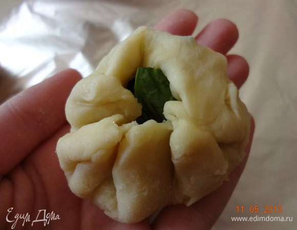 Раскатать шарик в лепешку, не тонко, начинка может порвать тесто и вытечь при выпечке. Взять немного листочков, свернуть их в шарик, выложить на лепешку и как бы обернуть тесто вокруг начинки, формируя мешочек, серединку защипнуть. Она может немного раскрыться в духовке, не страшно.