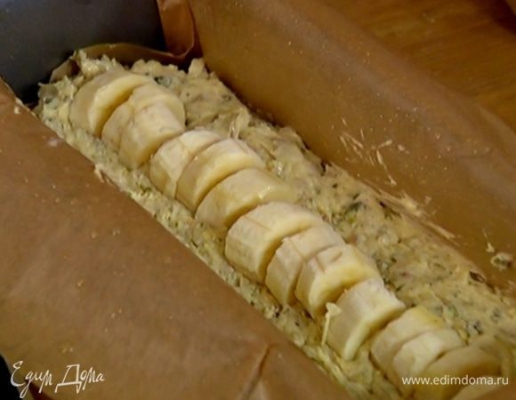 Продолговатую форму выстелить бумагой для выпечки, смазанной растительным маслом, выложить половину теста, по центру воткнуть кусочки бананов, утопив их в тесто ребром, затем выложить оставшееся тесто.