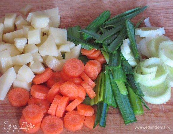 Белую часть лука-порея нарезать колечками, зелёную-полосками. Морковь нарезать кружочками, картофель-ломтиками. Зелень мелко порезать.