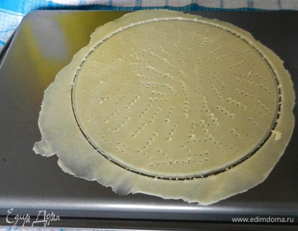 Когда тесто охладилось, включить духовку разогреваться на 200°С. Лист для выпечки перевернуть на обратную сторону и положить на полотенце, чтобы не скользил. На этом листе раскатать первый корж очень тонко, равномерно, и вырезать по форме круга (диаметр около 25 см). Излишки по краям не убирать с листа. Раскатанный корж попротыкать вилкой как можно чаще, чтобы не пузырилось. Если будет пузыриться в духовке, нужно корж вынуть и проколоть.