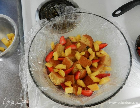 Скругленное блюдо застелить пленкой, оставив свешивающиеся края. Выложить на дно фруктово-ягодную смесь, затем слой из кусочков бисквита.