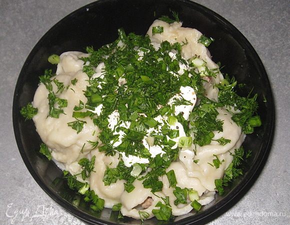 Выловить пельмени шумовкой. Добавить сливочное масло, сметану, свежемолотый перец и мелко нарубленную зелень. 