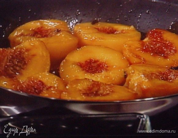 Персики помыть, разрезать на половинки. Обдать кипятком со стороны шкурки и удалить её. Сахарную пудру растопить на сковородке, залить апельсиновым соком,