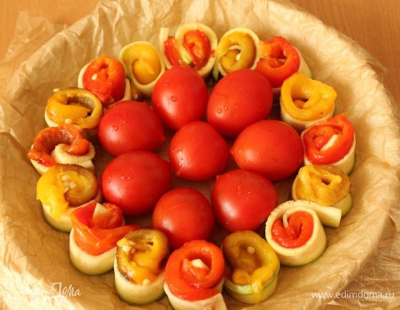 Выложить на разделочную доску ломтик кабачка, на него положить полоску перца и свернуть рулетом. Так поступить со всеми остальными ломтиками кабачка и перца. Форму для выпечки застелить пекарской бумагой и выложить рулетики. В оригинальном рецепте весь пирог состоит из рулетиков,  я решила слегка разбавить их помидорами. Посолить, поперчить и сбрызнуть маслом.