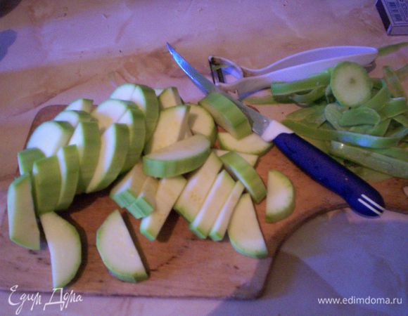 Очищаем кабачки от шкурки. Режем пополам вдоль, а потом нарезаем на полукружья шириной в 0,3 см. Добавляем нарезанные кабачки к обжаренному до золотистого цвета луку. Обжариваем их минут пять с открытой крышкой, перемешиваем, закрываем крышкой и уменьшаем вполовину огонь, чтобы теперь кабачки уже не обжаривались, а тушились. Пока тушатся кабачки, подготавливаем другие продукты.