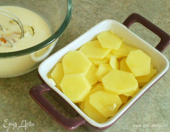 Пока томится мясо, картофель вымыть, очистить и нарезать тонкими ломтиками. Керамическую форму для запекания смазать маслом, уложить в нее картофельные ломтики, посолить и поперчить.