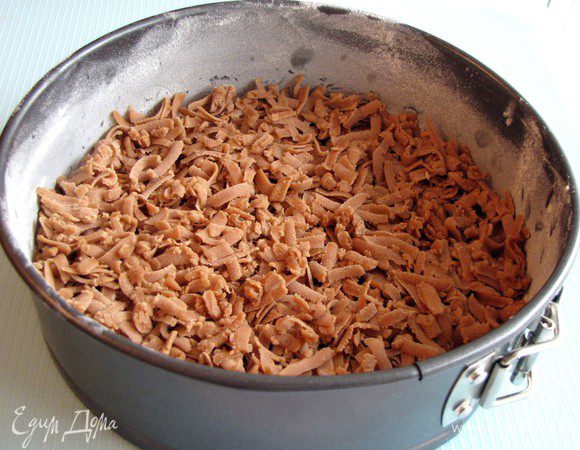 Форму для пирога смажьте маслом и посыпьте мукой. Тесто достаньте из холодильника и разделите на две равные части. Одну часть натрите на крупной терке и распределите по форме.