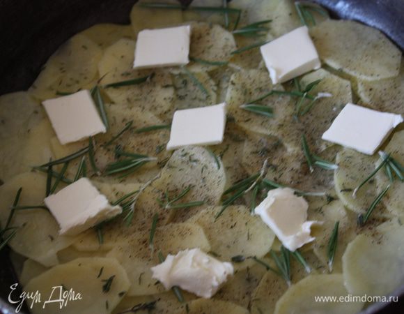Выкладываем третью часть картофеля на масло, солим, перчим. Добавляем листочки половины тимьяна и розмарина и кладем половину оставшегося масла, порезанного небольшими кусочками.
