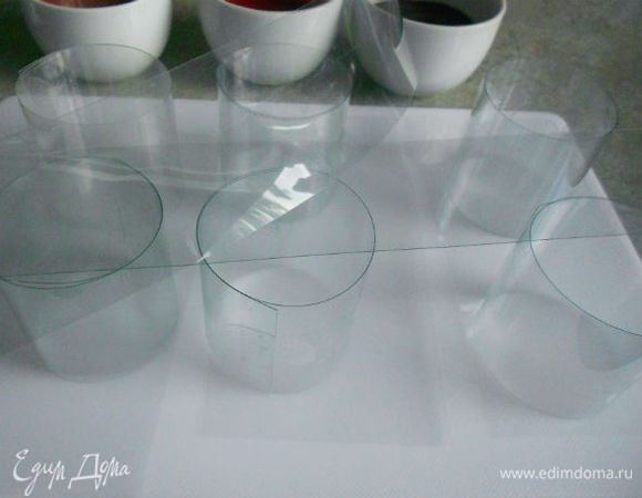 Если у вас есть десертные кольца, поместите внутрь их ацетатные полоски. Я обошлась только полосками: оборачивала их вокруг подходящего стаканчика и закрепляла скотчем. (Он потом просто рассекается тонким ножом.) Очень даже прочно получилось. Большую разделочную доску накройте либо фольгой, либо такими же пластиковыми полосками и на них установите свои  импровизированные или настоящие кольца.