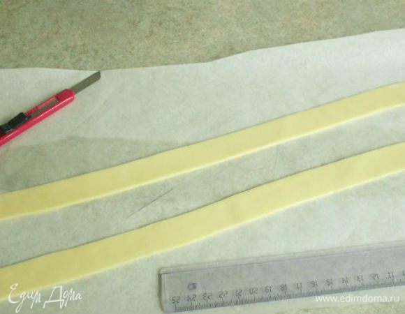 Не разминать долго массу в руках ! Она  итак стала гладкой и мягкой. Скатать её колбаской, поместить между 2 листами бумаги для выпечки и раскатать скалкой в пласт. Снять верхнюю бумагу. Используя линейку и острый тонкий нож, вырезать 2 полоски 30 х 2.5  см. Если они очень мягкие, охладите их несколько минут в холодильнике.