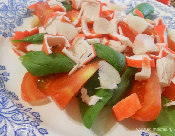 Помидор нарезать тонкими ломтиками, выложить на блюдо, между дольками     выложить листья шпината, сверху накрошить крабовое мясо или палочку.