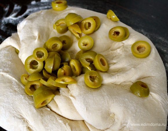 Выложить тесто на присыпанную мукой поверхность и добавить постепенно в него оливки.