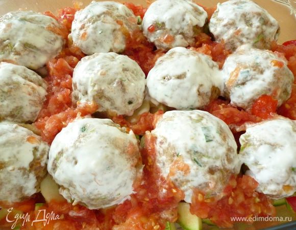 Из фарша формуем шарики и выкладываем их на овощи. Затем ложкой распределяем натертые томаты. Каждый мясной шарик смазать сметаной. Форму накрыть крышкой .Запекать в духовке 40 минут с момента закипания.