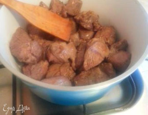 Теперь подготовим кастрюлю или глубокую сковороду, где мы продолжим готовить блюдо. У меня керамическая кастрюля. На дно выкладываем баранину. В блюде, где мясо лежало, собрался сок: его я тоже вливаю в кастрюлю.