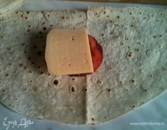 Кладем половинку лавашика на стол , кладем на серединку пластик колбаски, поверх пластик томата, посолить его, поперчить, поверх положить сыр.