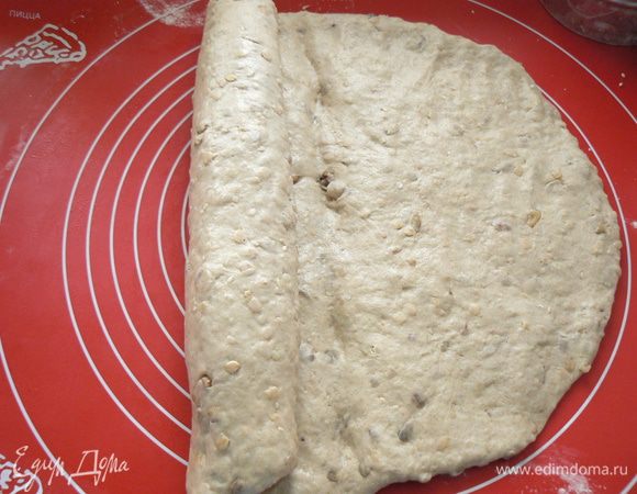 Выброженное тесто выложите на подпыленную мукой рабочую поверхность. Раскатайте его скалкой или расплющите руками в прямоугольник и сверните в плотный рулет, запечатывая на каждом витке ребром ладони. Защипните шов. 
