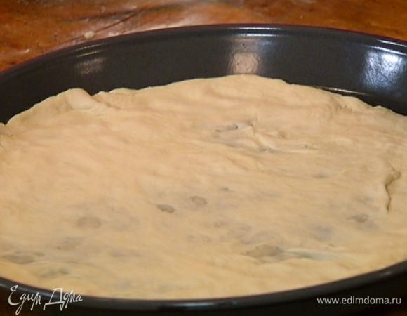Большую форму с невысокими бортиками прогреть в духовке. Рабочую поверхность посыпать оставшейся мукой, раскатать из теста тонкий пласт и выложить его в разогретую форму.