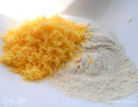 Муку (сначала не всю,так как много зависит от сорта сыра,его мягкости) соединить с разрыхлителем и всыпать сыр.
