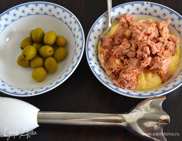 Тунца достать из банки, дать стечь лишней жидкости, поломать вилкой. С помощью погруженного блендера (или в миксере) измельчить тунца с майонезом, кетчупом, оливками (отложите одну для украшения), добавив чуть-чуть оливкового масла. 