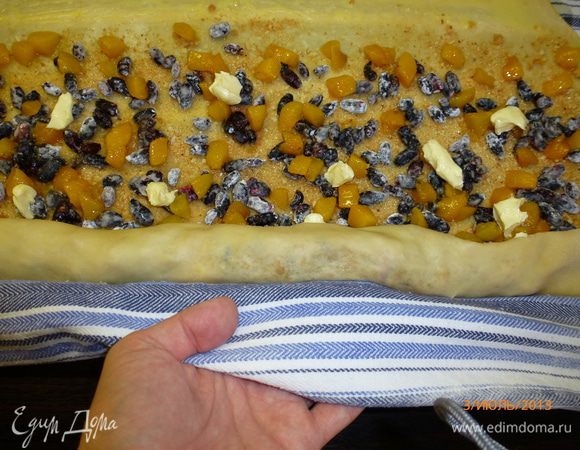 Противень смазываем маслом и присыпаем мукой. С помощью полотенца сворачиваем рулет, защипываем кончики, переносим на противень швом вниз. 