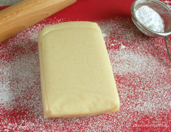 Рабочую поверхность посыпьте сахарной пудрой и раскатайте на ней марципан в прямоугольник 40 х 20 см. Он должен быть достаточно большой, чтобы обернуть пирог полностью, оставляя немного с краёв для обрезания. Толщина его должна быть около 5 мм.