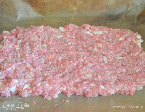 на противень выложить коврик для выпечки или бумагу, смазанную маслом. Распределить по ней половину фарша в форме прямоугольника