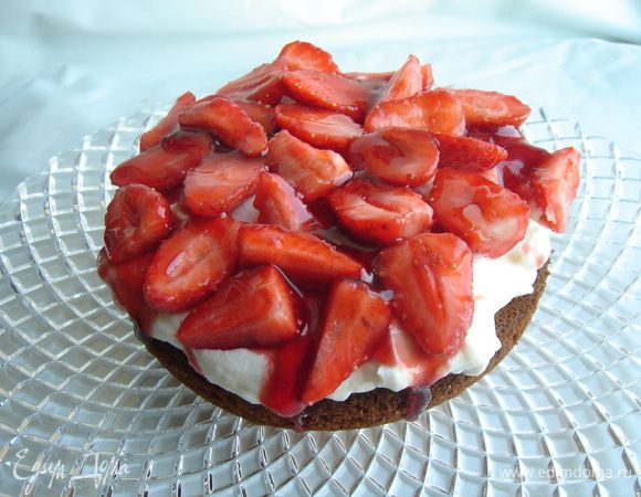 Чтобы собрать кекс, необходимо выложить один корж дном вверх на блюдо, пригодное для подачи на стол. Покрыть корж сливочным кремом, затем разложить ягоды и полить их сиропом. Прикрыть вторым коржом дном вниз. Засыпать кекс сахарной пудрой и убрать в холодильник на 1-2 часа. Перед подачей украсить клубникой.