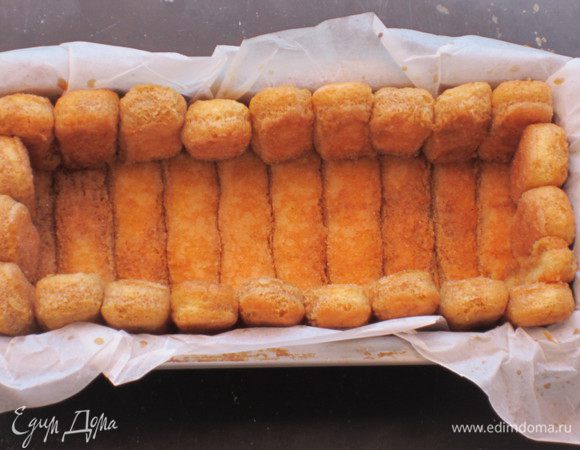 Сварить кофе, добавить ром и сахар по вкусу, пропитать печенье. Прямоугольную форму застелить пергаментом. Выложить печеньем бортик и дно формы.