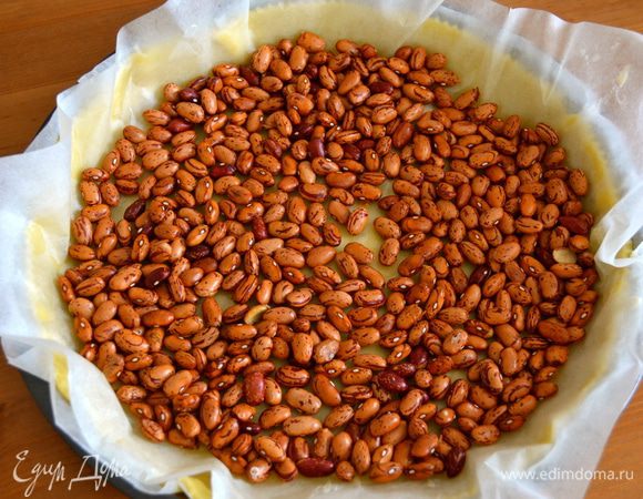 Накройте основание для пирога пекарской бумагой (или фольгой) и выложите фасоль (горох или другие используемые вами «утяжелители»). Выпекайте в разогретой духовке 15 минут.