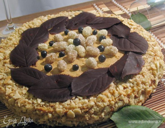 Края и часть верха обсыпаем измельченной смесью из орехов и обрезков коржей. Украшаем шоколадными листочками и фруктами или по вашему желанию. 