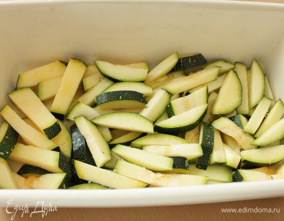 На дно формы для запекания налить оливковое масло. Кабачок нарезать вдоль пластинами и затем брусочками, распределить ровным слоем, слегка посолить.