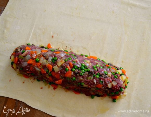 Поверните пласт раскатанного теста длинной стороной к себе и выложите мясо, сформировав из него подобие длинной котлеты.  