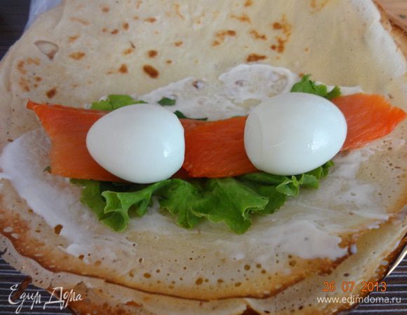 Половину блинчика смазать тонким слоем сметаны, положить салатный лист, две пластинки рыбы, два яйца, свернуть плотно прижимая начинку в рулет. Так же завернуть остальные. Можно разрезать на две, три части, можно оставить целым.