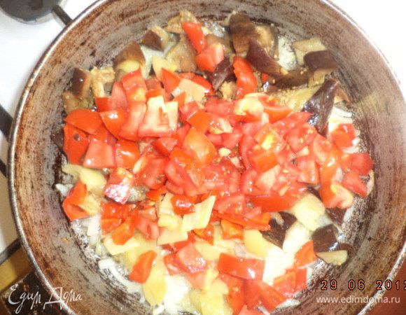 Добавить баклажан, перцы и нарезанные кубиками помидоры. Перемешать. Протушить на маленьком огне 5 минут, периодически перемешивая. Добавить чеснок и рубленую зелень, посолить, поперчить, перемешать.