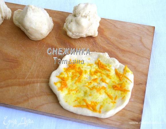 С утра достаём тесто и сразу делим его на 8 частей. Разминаем прямо руками шарик в лепёшку. Если используете цедру в качестве начинки, предварительно вымойте апельсин и натрите цедру на тёрке. Кладём на лепёшку немного начинки. У меня ещё часть булочек были с корицей.