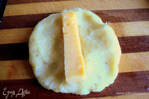 Добавить 1 яйцо, муку и крахмал, соль и перец по вкусу, хорошо перемешать. Сыр нарезать брусочками. Оставшееся яйцо взбить с солью. Из картофельной массы сформировать мокрыми руками небольшие лепешки, положить по центру сыр.