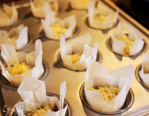 Духовку разогреть до 200*С. В форму для маффинов/кексов выложить бумажные капсулы и наполнить из на 3/4 тестом. Присыпать кексы тёртым сыром, а затем дроблёнными орешками или семечками. Выпекать около 30 минут.