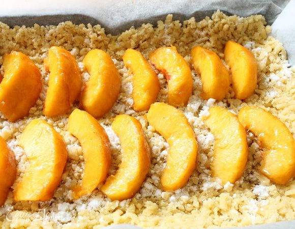 У персиков удалить косточки и кожицу,нарезать их дольками и распределить ровным слоем