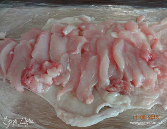На разделочную доску выложить пищевую пленку в 5 слоев, не меньше. Распределить на ней кожицу, на ней ломтики филе грудки.