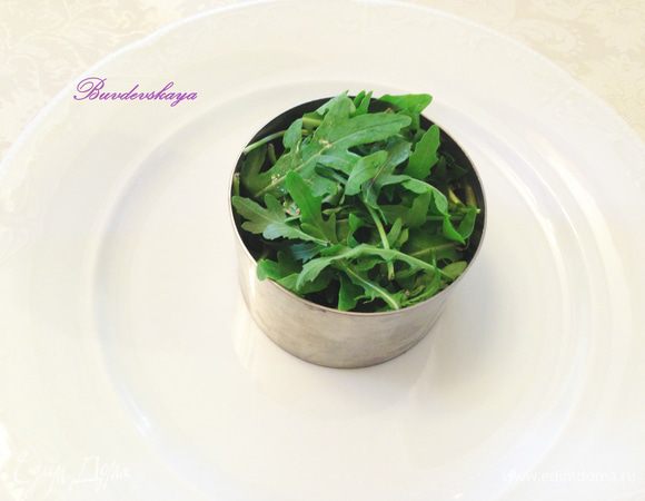 Руколу вымыть, обсушить. На центр большой тарелки поставить кулинарное кольцо и выложить в него руколу, слегка утрамбовав. Если нет кольца, то можно выложить руколу аккуратной горкой.