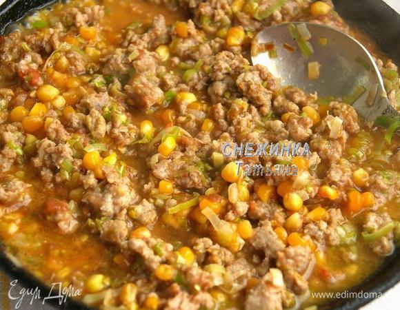 Добавляем фарш, помешивая, держим на огне 5 минут. Помидор разрезаем пополам и натираем на терке со стороны среза, таким образом кожица остаётся и получается по типу томатного пюре. Добавляем в сковороду кукурузу и томатное пюре. 
