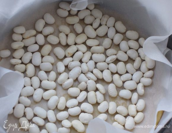 Разделить тесто на две части. Одну часть теста раскатать толщиной 3-4 мм и выложить в форму с пергаментом. Тесто наколоть вилкой, положить лист пергамента и сверху выложить фасоль. Выпекать в разогретой до 180 °С духовке 10 минут.