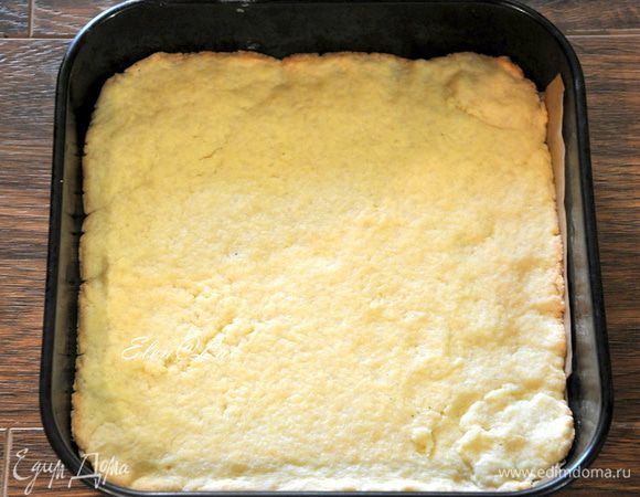 Тесто разделите на две части. Раскатайте одну часть в прямоугольник 26х35. Раскатанный пласт аккуратно переложите на противень застеленный пергаментом или в прямоугольную форму. Тесто наколите вилкой. Выпекать корж в заранее разогретой до 180С духовке 10 минут.