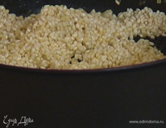 Вернуть сотейник на огонь, выложить в него измельченный лук, всыпать рис. Сделать тостатуру: прогревать рис, постоянно помешивая, в течение 1‒2 минут, пока зерна не станут прозрачными.
