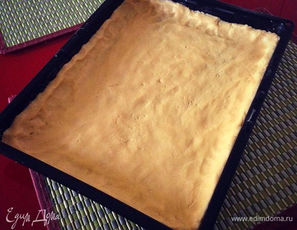 Противень смазать маслом и слегка присыпать мукой, тесто равномерно распределить по поверхности противня, по бокам сформировать бортики. 