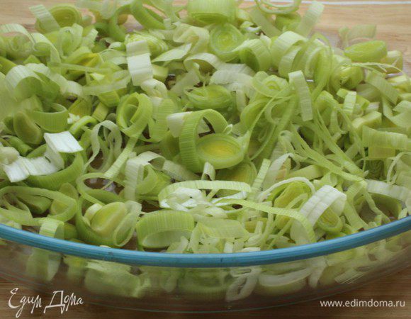 Порей (белую часть) нарезать тонкими кольцами и выложить в смазанную оливковым маслом форму для запекания.