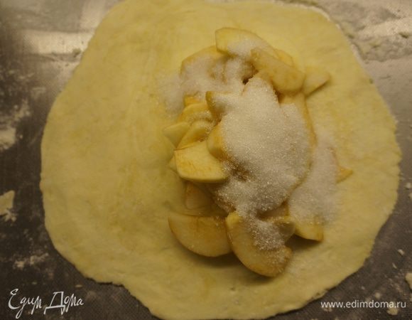 Достать тесто из холодильника, разделить на 5 - 6 частей. 
Каждую часть раскатать в блинчик, не очень тонко. А затем по принципу лепки вареников, на одну половину блина положить начинку из яблок и посыпать сахарным песком - 1-2 десертных ложки в каждый пирог. 