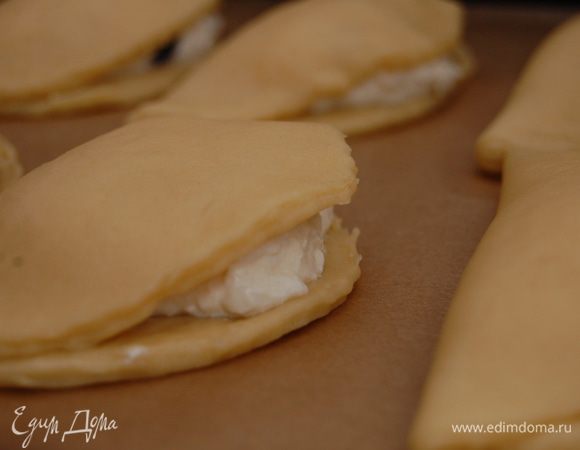 Раскатать тесто (толщина не более 5 мм) и вырезать кружки диаметром 12см.  В центр каждого круга выложить по 1 ст.л начинки и сложить пополам.  Защипнуть сочники как вареники, буквально по 1 см от каждого края. Складываем сочни на противень застеленный пекарской бумагой, смазываем желтком и выпекаем при температуре 180 градусов до готовности. В моей духовке – это ровно 17 минут.  Важно не передержать иначе они станут сухими и невкусными.